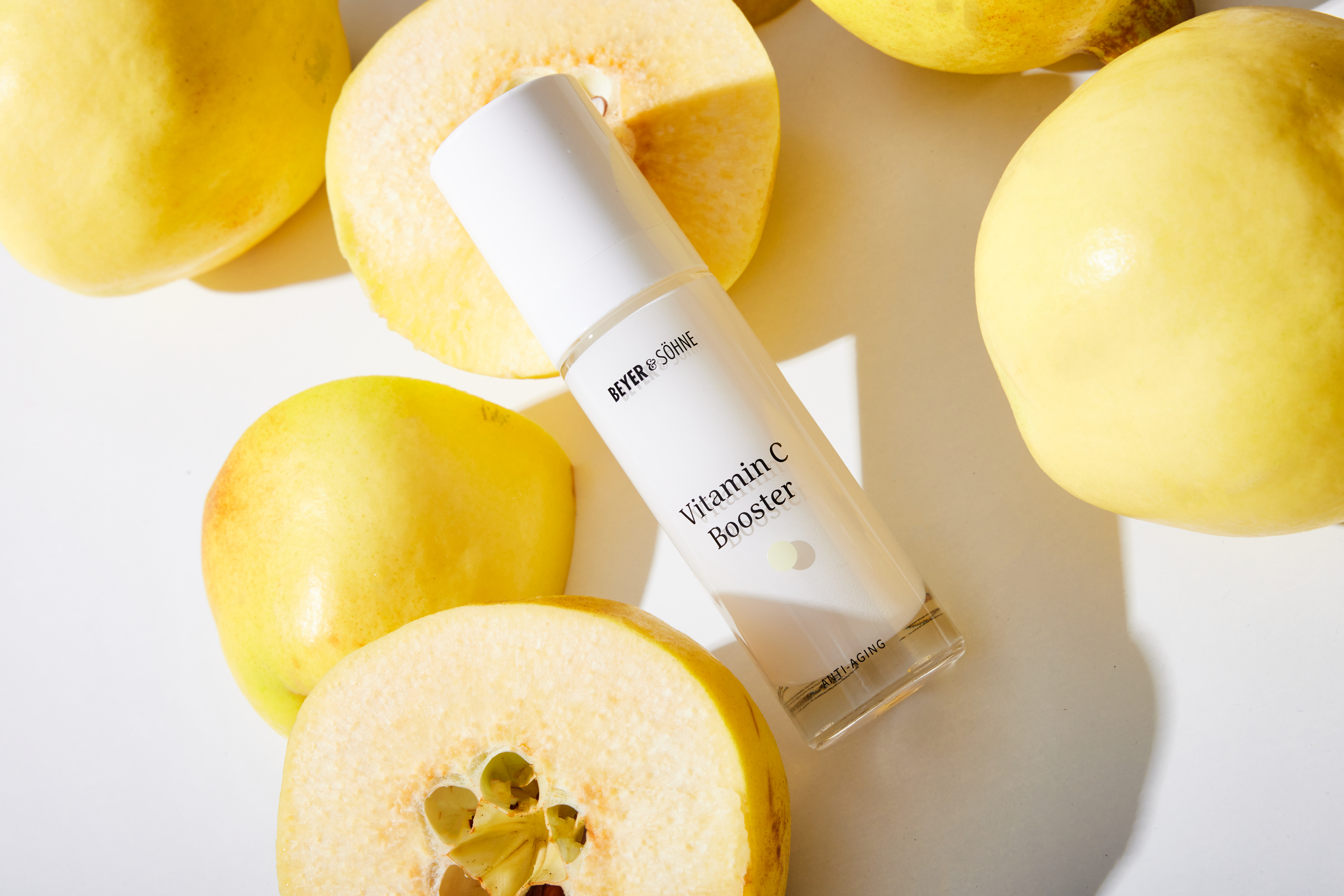 Vitamin C Booster von Beyer & Söhne in edler weißer Glasflasche umgeben von gelben Früchten